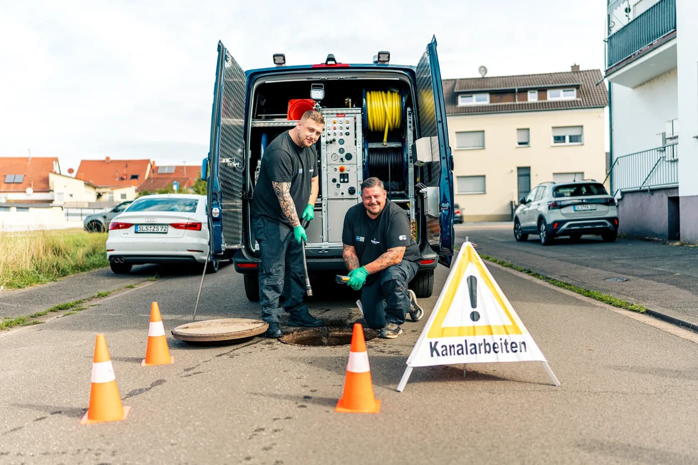 Monteure der Müller GmbH bei der Kanalspülung am offenen Schacht, mit Warnschild Kanalarbeiten