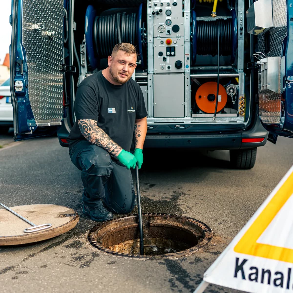Monteur der Müller GmbH am geöffneten Hausanschlussschacht, mit Warnschild Kanalarbeiten
