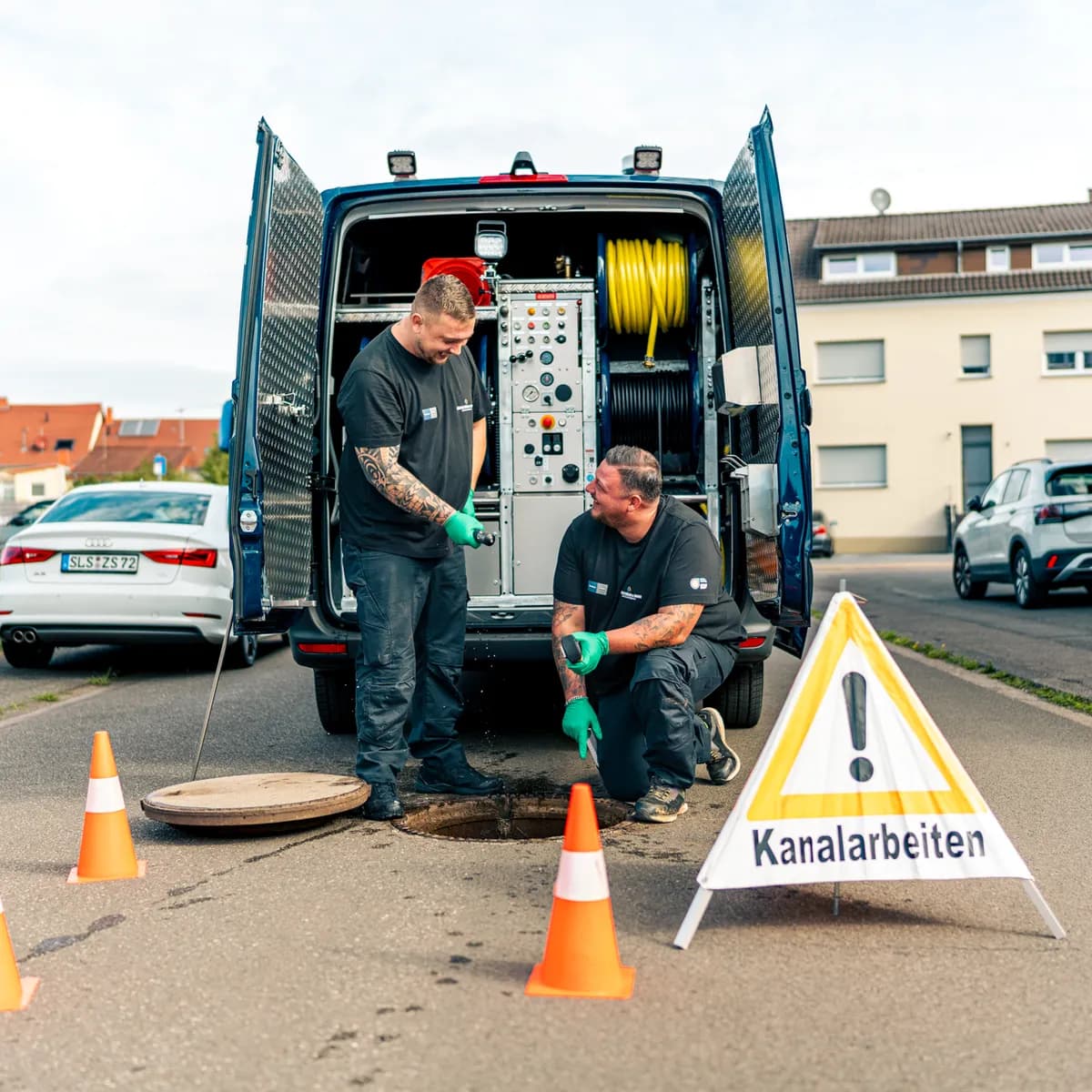 Zwei Monteure der Müller GmbH bei der Hochdruckspülung am offenen Kanalschacht an der Straße
